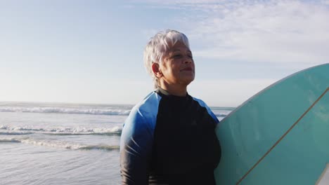 Ältere-Afroamerikanische-Frau,-Die-Mit-Einem-Surfbrett-Am-Strand-Spaziert