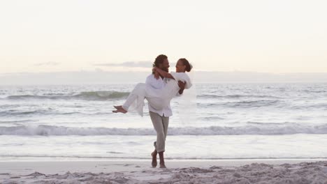African-american-couple-in-love-getting-married,-man-carrying-woman-on-the-beach-at-sunset