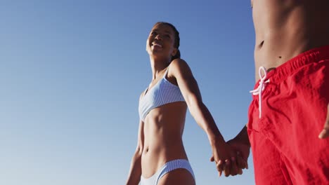 African-american-couple-in-swimwear-smiling-and-holding-hands-on-the-beach