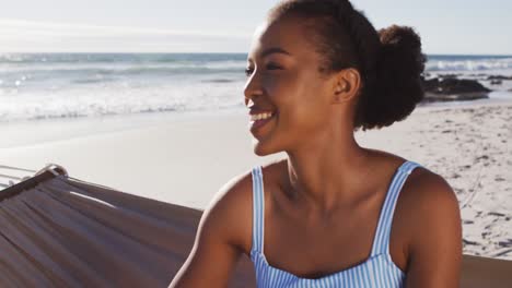 Nahaufnahme-Einer-Afroamerikanischen-Frau,-Die-Lächelt,-Während-Sie-Auf-Einer-Hängematte-Am-Strand-Sitzt