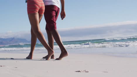 Unterer-Teil-Eines-Afroamerikanischen-Paares,-Das-Sich-Umarmt-Und-Am-Strand-Spazieren-Geht