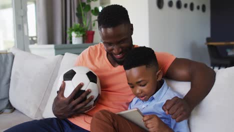 Afroamerikanischer-Vater-Und-Sohn-Jubeln-Gemeinsam,-Während-Sie-Zu-Hause-Sport-Auf-Einem-Digitalen-Tablet-Schauen