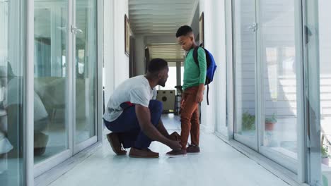 African-american-father-helping-his-son-with-tying-shoes-in-hallway