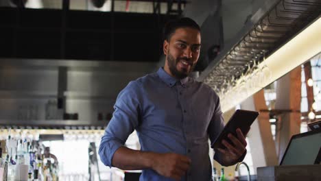 Portrait-of-mixed-race-male-cafe-owner-using-tablet-and-looking-to-camera