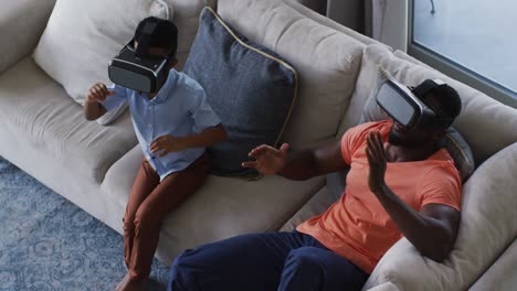 Afroamerikanischer-Vater-Und-Sohn-Nutzen-Gemeinsam-VR-Headsets-Auf-Einer-Couch