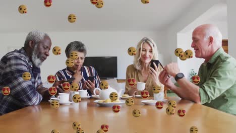 Face-emojis-floating-against-two-senior-diverse-couples-using-smartphone-while-having-coffee