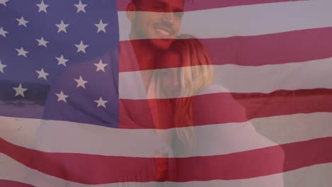 Amerikanische-Flagge-Weht-Gegen-Ein-Kaukasisches-Paar,-Das-Sich-Am-Strand-Umarmt