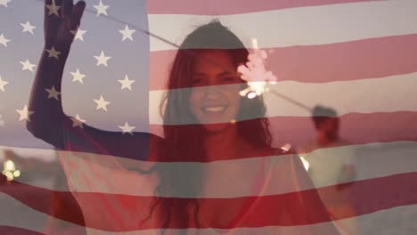 Animation-Einer-Amerikanischen-Flagge,-Die-über-Einer-Gruppe-Von-Frauen-Mit-Wunderkerzen-Am-Strand-Weht