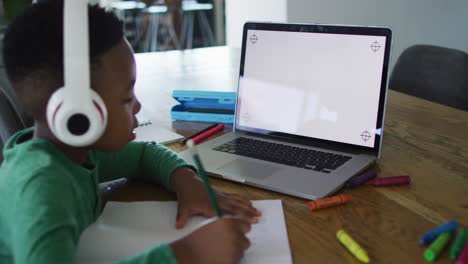 Afroamerikanischer-Junge,-Der-Einen-Videoanruf-Auf-Einem-Laptop-Mit-Kopierplatz-Führt,-Während-Er-Zu-Hause-Hausaufgaben-Macht