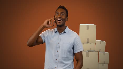Animation-of-smiling-man-talking-on-smartphone-with-stacks-of-boxes-on-orange-background