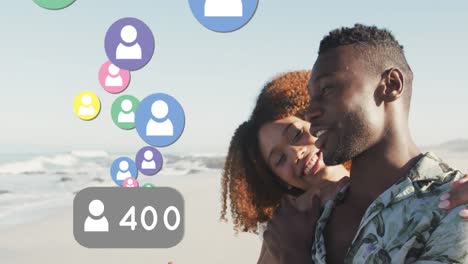 Profile-icons-with-increasing-numbers-floating-against-african-american-couple-smiling-on-the-beach