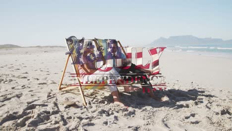 Independence-day-text-against-senior-caucasian-couple-sitting-on-deck-chairs-at-beach