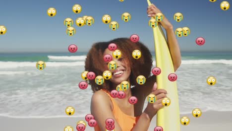 Animation-Von-Social-Media-Emojis-über-Einer-Lächelnden-Frau,-Die-Ein-Surfbrett-Am-Strand-Hält