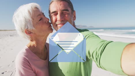 Animation-of-social-media-email-icon-over-senior-woman-kissing-her-husband-on-beach