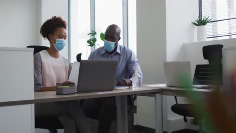 Diverse-businessman-and-businesswoman-in-face-masks-discussing-in-office