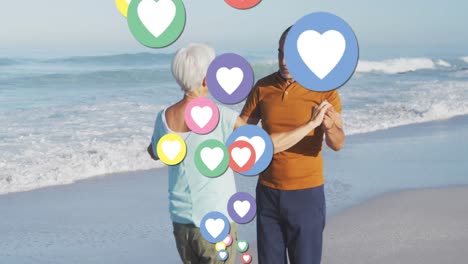 Animation-of-heart-digital-icons-over-senior-couple-dancing-on-beach