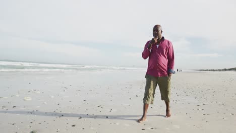 African-american-senior-man-walking-on-a-beach-rubbing-his-chin-and-looking-at-the-sea