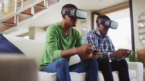 Afroamerikanische-Teenager-Zwillingsbrüder-Sitzen-Auf-Der-Couch,-Benutzen-VR-Headsets-Und-Spielen-Computerspiele