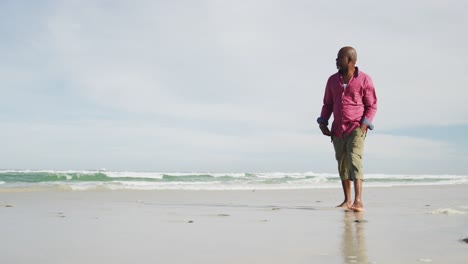 Afroamerikanischer-älterer-Mann,-Der-An-Einem-Strand-Spaziert-Und-Auf-Das-Meer-Blickt