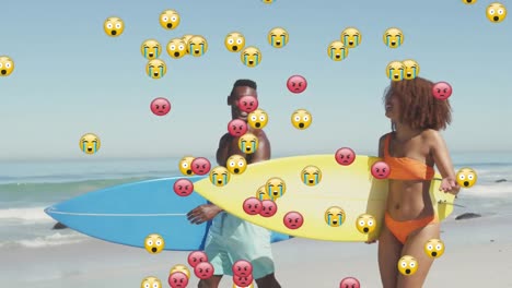 Animation-Von-Social-Media-Emojis-über-Einem-Lächelnden-Paar,-Das-Surfbretter-Am-Strand-Hält