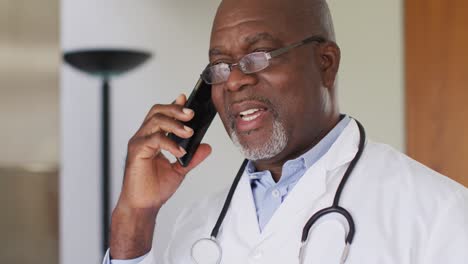 African-american-senior-male-doctor-wearing-white-coat-talking-on-smartphone