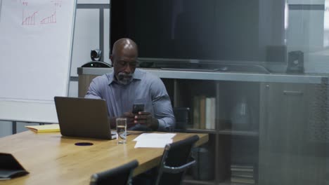 African-american-businessman-using-smartphone-and-laptop-in-conference-room-at-office