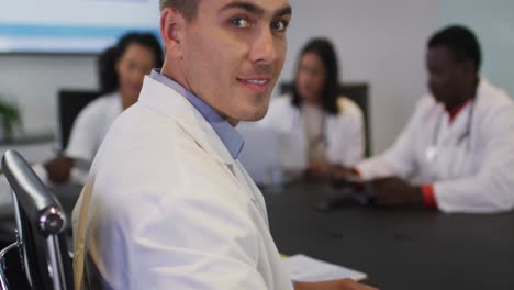 Portrait-of-caucasian-male-doctor-sitting-in-meeting-room-looking-to-camera-smiling