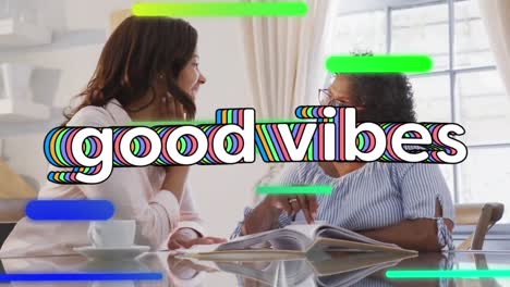 Animation-of-good-vibes-text-over-two-women-talking-and-looking-at-photos-at-home