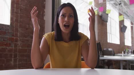 Mixed-race-businesswoman-sitting-at-desk-having-video-call-gesturing
