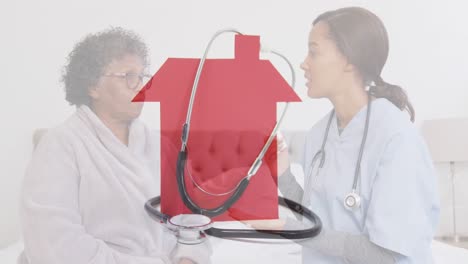 Animation-of-stethoscope-on-red-house-over-female-doctor-with-senior-woman-talking