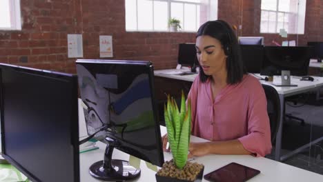 Mixed-race-businesswoman-wearing-headset-sitting-at-desk-having-video-call