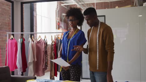 African-american-male-and-female-fashion-designers-in-discussion-at-work-looking-at-document