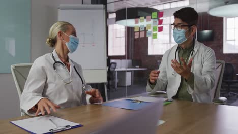Diverse-male-and-female-doctors-wearing-face-masks-brainstorming-in-meeting-room