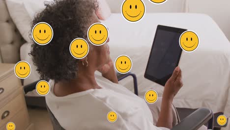 Animation-of-digital-emoji-icons-over-senior-woman-using-tablet-at-home