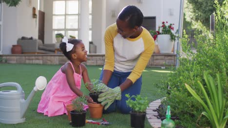 Happy-african-american-mother-and-daughter-gardening,-planting-plants-in-garden