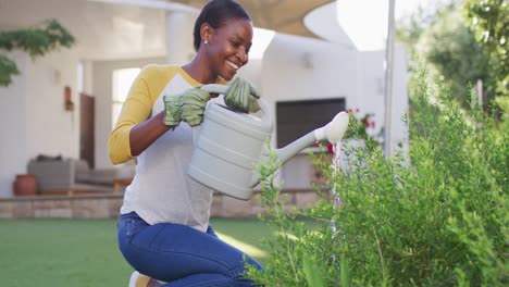 Happy-african-amercian-woman-gardening,-watering-plants-in-garden