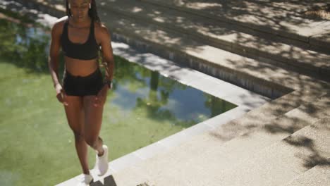African-american-woman-wearing-wireless-earphones-exercising-outdoors-jumping-on-stairs-in-the-city