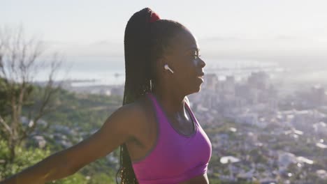 African-american-woman-wearing-wireless-earphones-stretching-her-arms-outdoors