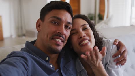 Romantic-hispanic-couple-embracing-sending-kisses-on-sofa-in-living-room