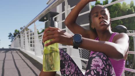 Mujer-Afroamericana-Cansada-Con-Una-Botella-De-Agua-Tomando-Un-Descanso-De-Correr-En-El-Puente-De-La-Ciudad