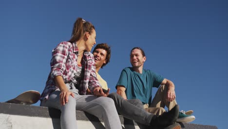 Happy-caucasian-woman-and-two-male-friends-sitting,-laughing-and-spending-time-together-on-sunny-day