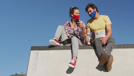 Caucasian-woman-and-man-friends-wearing-face-mask,-sitting-and-using-smartphone