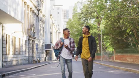 Two-happy-mixed-race-male-friends-walking-and-talking-with-backpacks