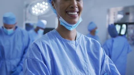 Portrait-of-mixed-race-female-doctor-standing-in-operating-theatre-smiling-to-camera