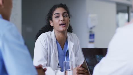 Asian-female-doctor-wearing-lab-coat-sitting-and-addressing-hospital-colleagues-at-a-meeting