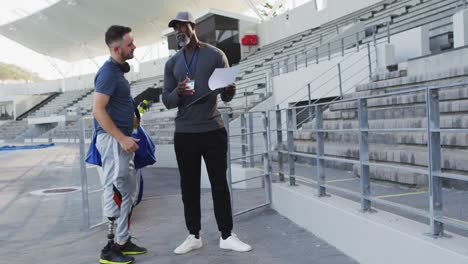 Diverse-male-coach-and-disabled-athlete-with-prosthetic-leg-talking-during-training-session