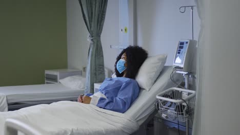Portrait-of-african-american-female-patient-wearing-face-mask-lying-on-hospital-bed