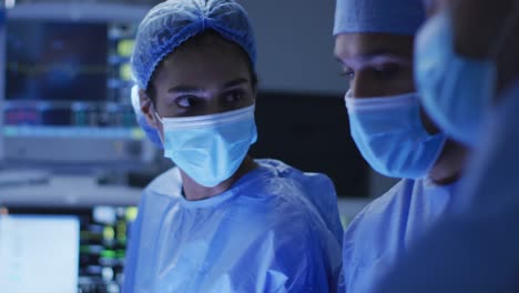 Mixed-race-surgeons-wearing-protective-clothing-discussing-in-operating-theatre