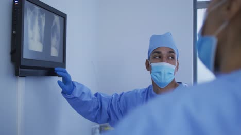 Mixed-race-male-surgeon-wearing-protective-clothing-presenting-x-ray-on-screen
