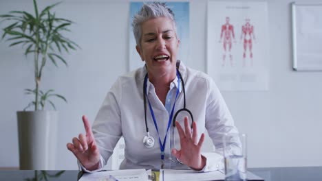 Caucasian-female-doctor-at-desk-talking-and-gesturing-during-video-call-consultation